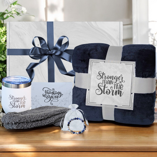 Women's self-care gift box with cozy navy blue blanket, blue socks, blue Sodalite natural stone bracelet, white 18 oz tumbler and thinking of you card – perfect get well gift for her. Featuring Stronger Than the Storm Theme