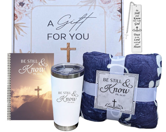 A gift set containing a spiral journal, a metal bookmark with Bible verses, a white insulated tumbler with 'Be Still & Know' text, and a lightweight blue throw blanket with Bible verses, all packaged in a gift box with a cross design.