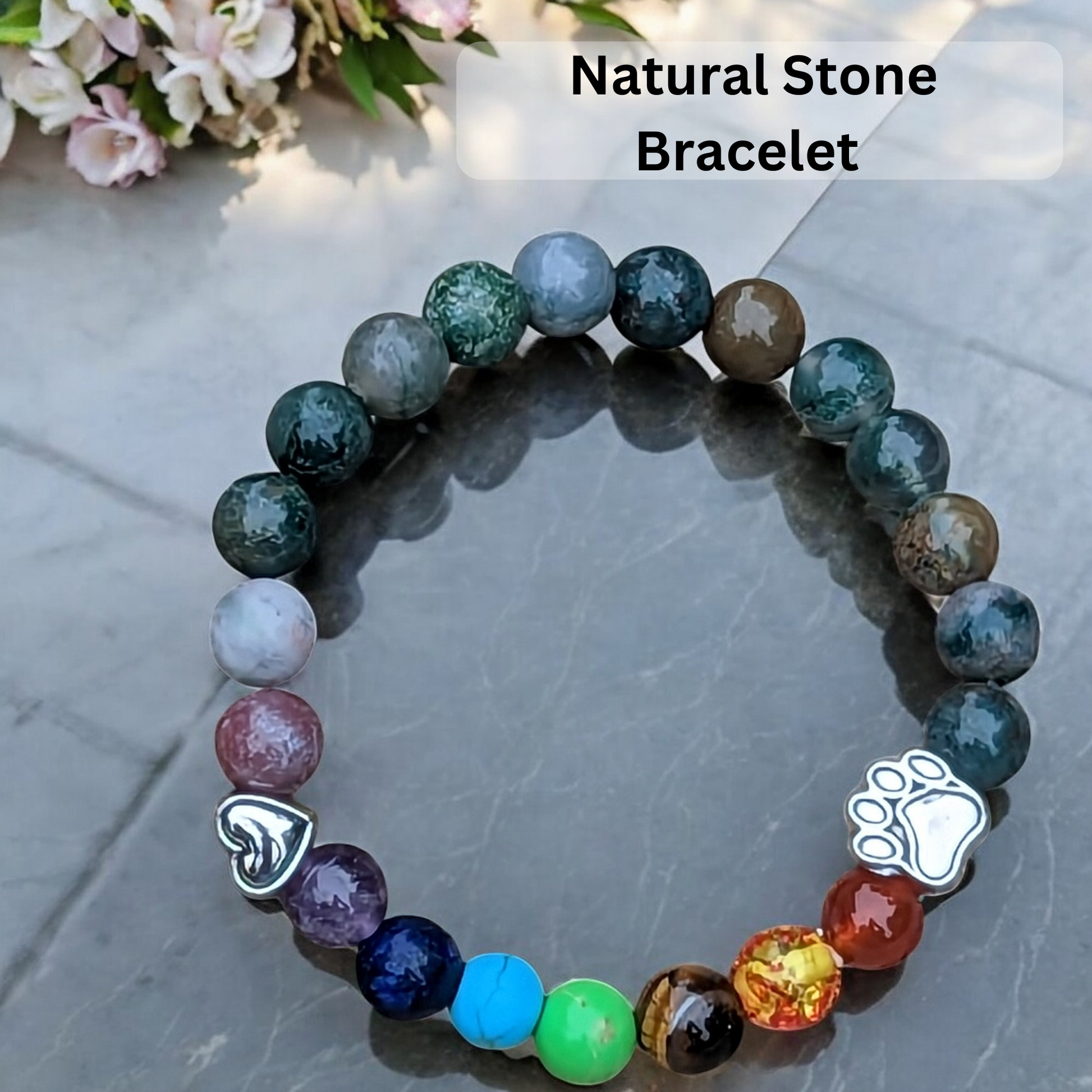 Natural stone bracelet with paw charm on a reflective surface, flowers in the background