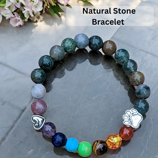 Natural stone bracelet with paw charm on a reflective surface, flowers in the background