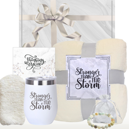 A gift box for women containing an ivory plush blanket, a white insulated wine tumbler with a lid, a natural stone bracelet, ivory socks and a 'Thinking of You' card, all ready to be gifted. All presented with a ‘Thinking of You’ and ‘Stronger Than The storm’ theme